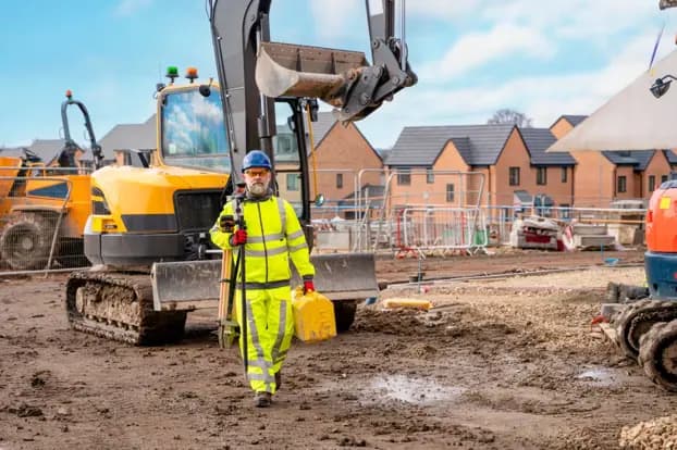 Excavator and worker preparing the ground beside new brick houses